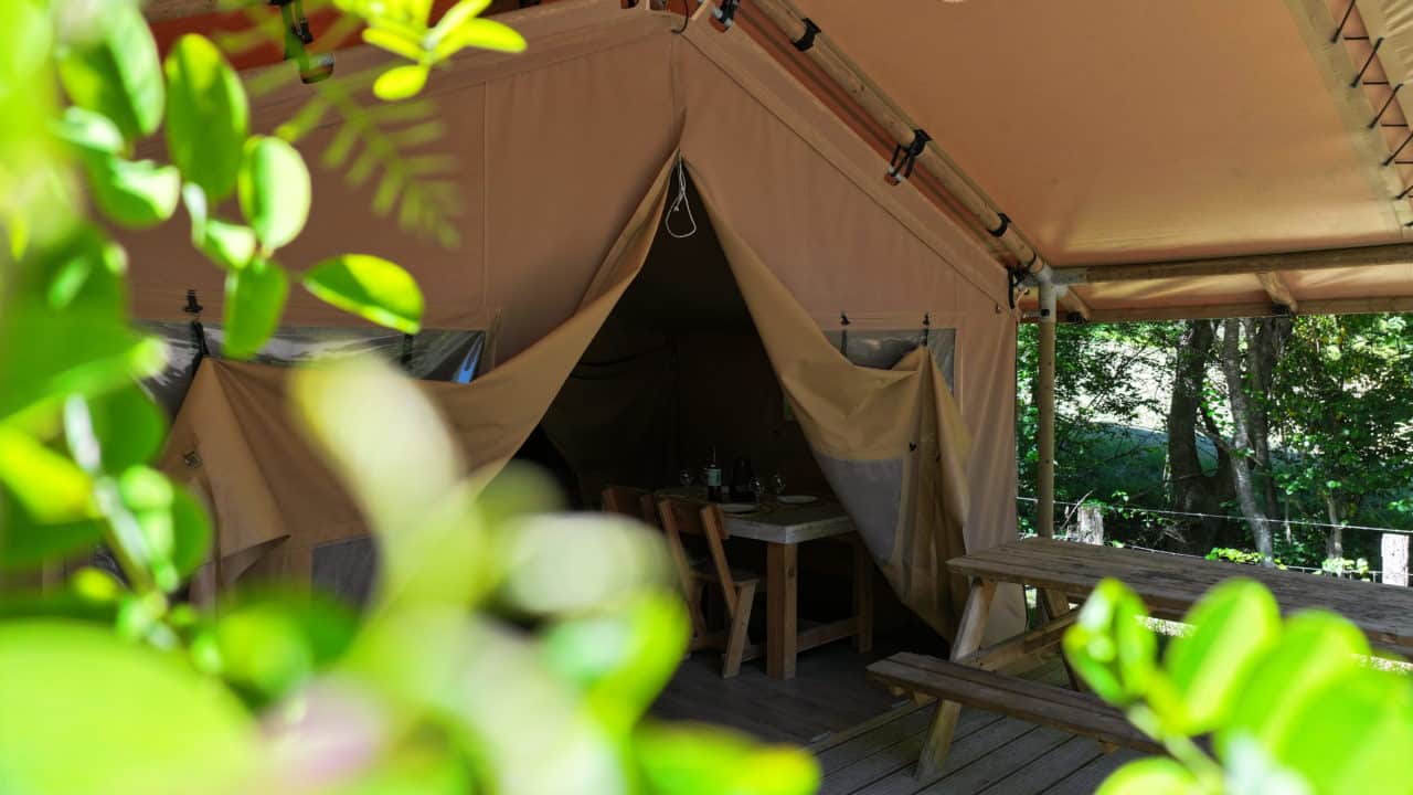 Lodge en bois avec sa terrasse couverte, à l'ombre des arbres du camping La Serre en Ariège