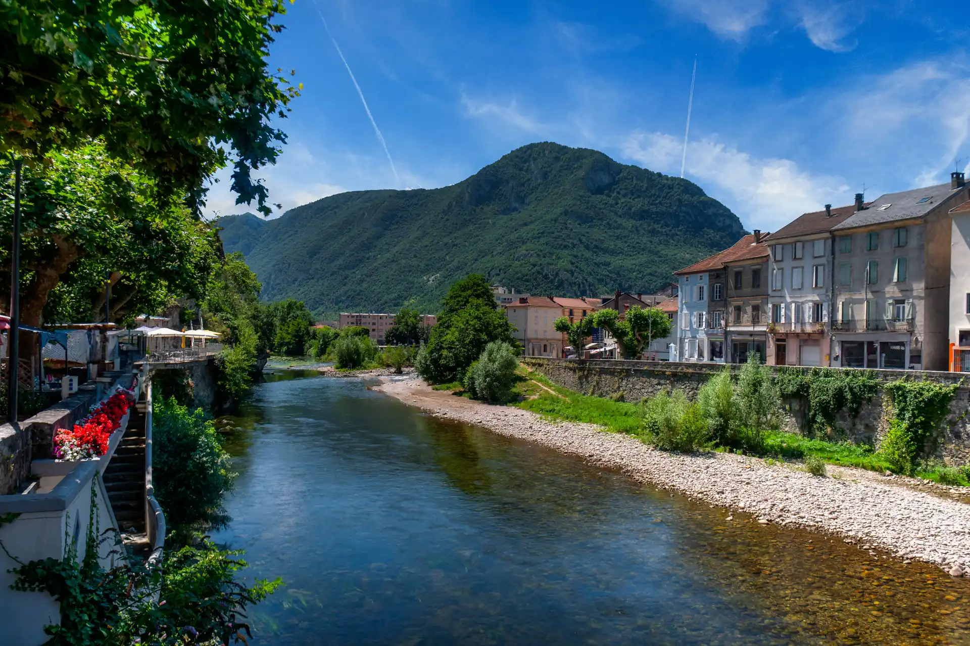 L'Ariège traverse Tarascon-sur-Ariège entre une berge de galets et des façades anciennes, au pied d'une montagne boisée
